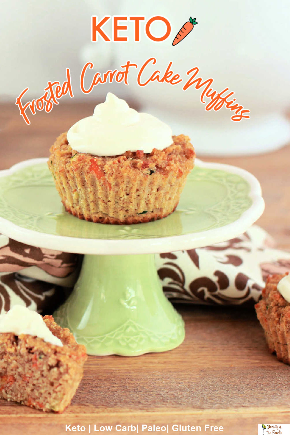 A frosted carrot cake muffin on a small pedestal with muffins in the background.