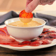 A bowl of chili queso dip with abaked pepperoni being dipped into it.