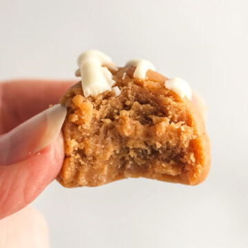 A hand holding a peanut butter cookie fat bomb with a bite out of it.