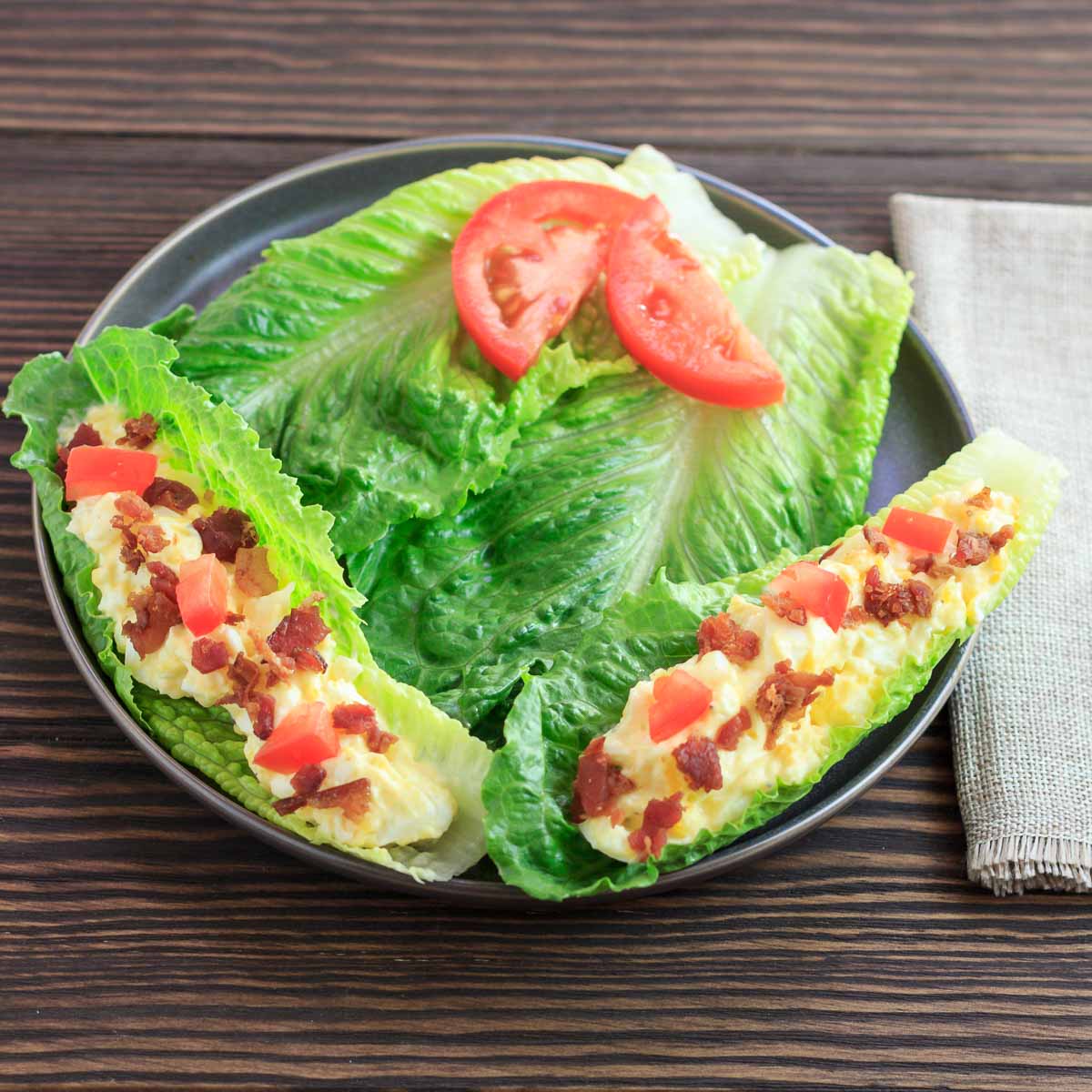 Egg salad bacon and tomato in 2 lettuce boats.