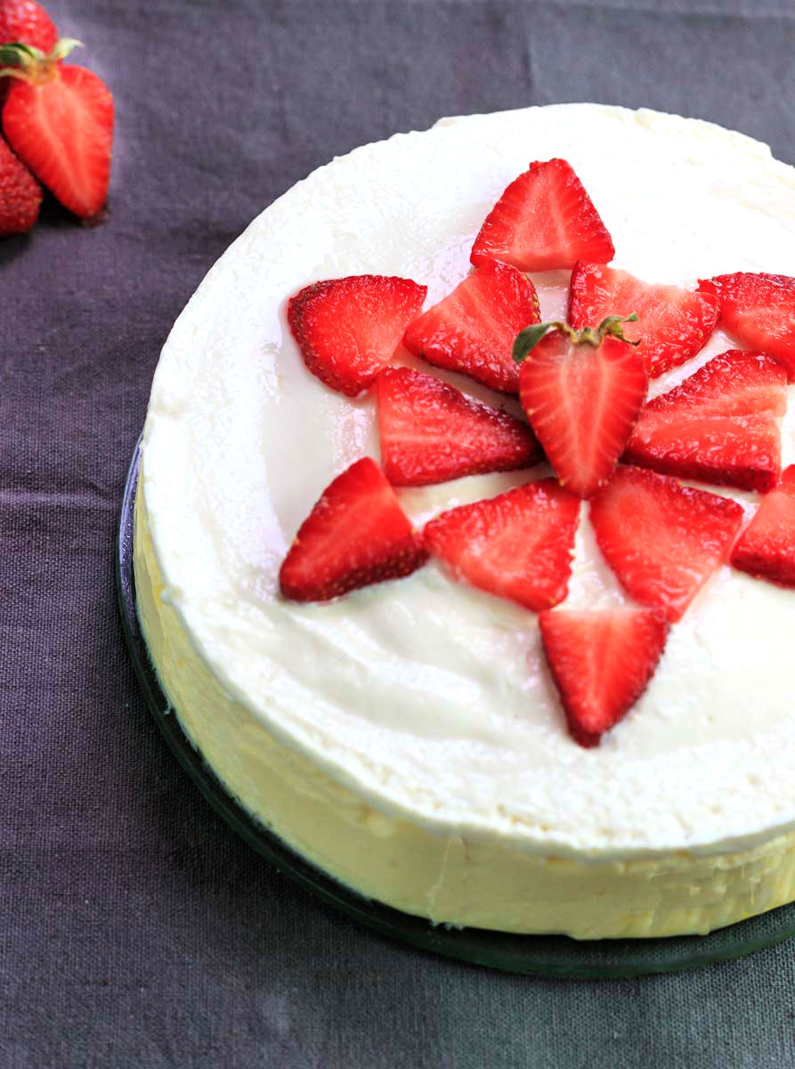 A whole keto cheesecake with sliced strawberries.