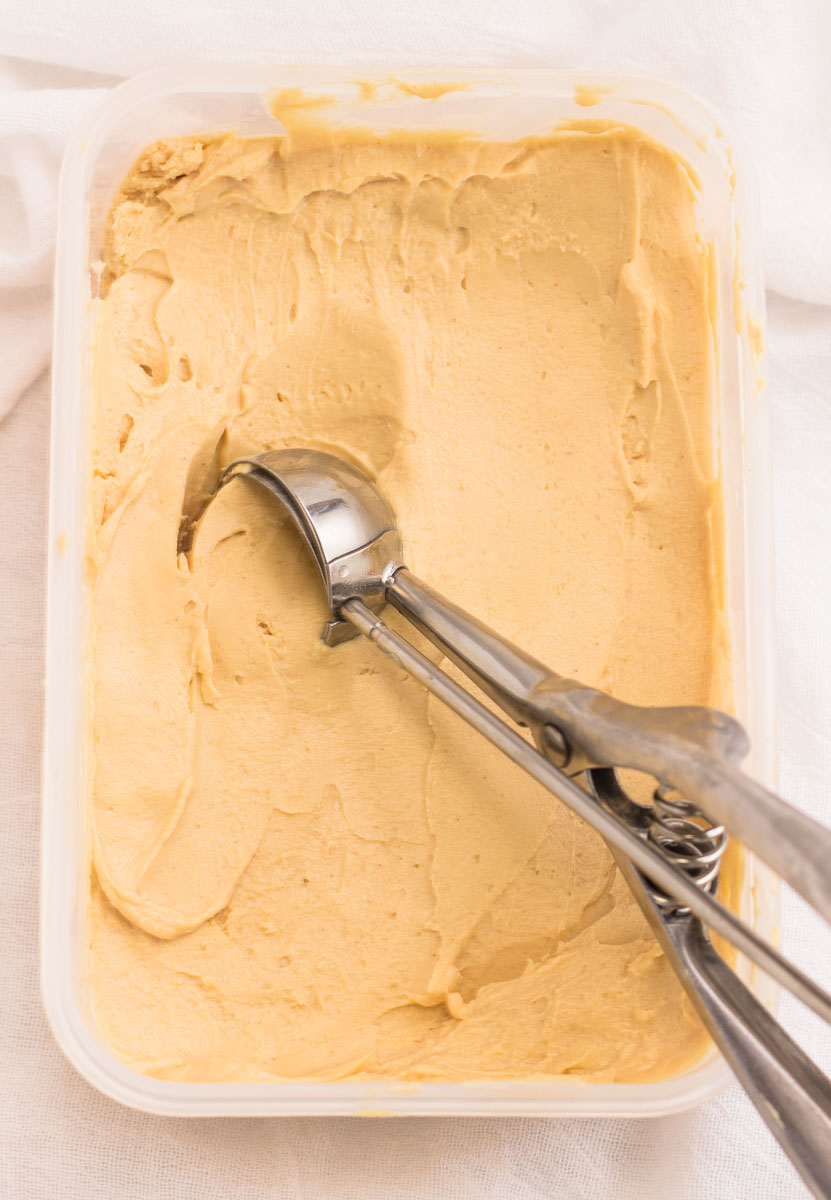 Scooping out a scoop of peanut butter frozen yogurt from a container.