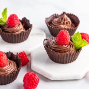 Four chocolate cups filled with chocolate mousse and topped with a raspberry.