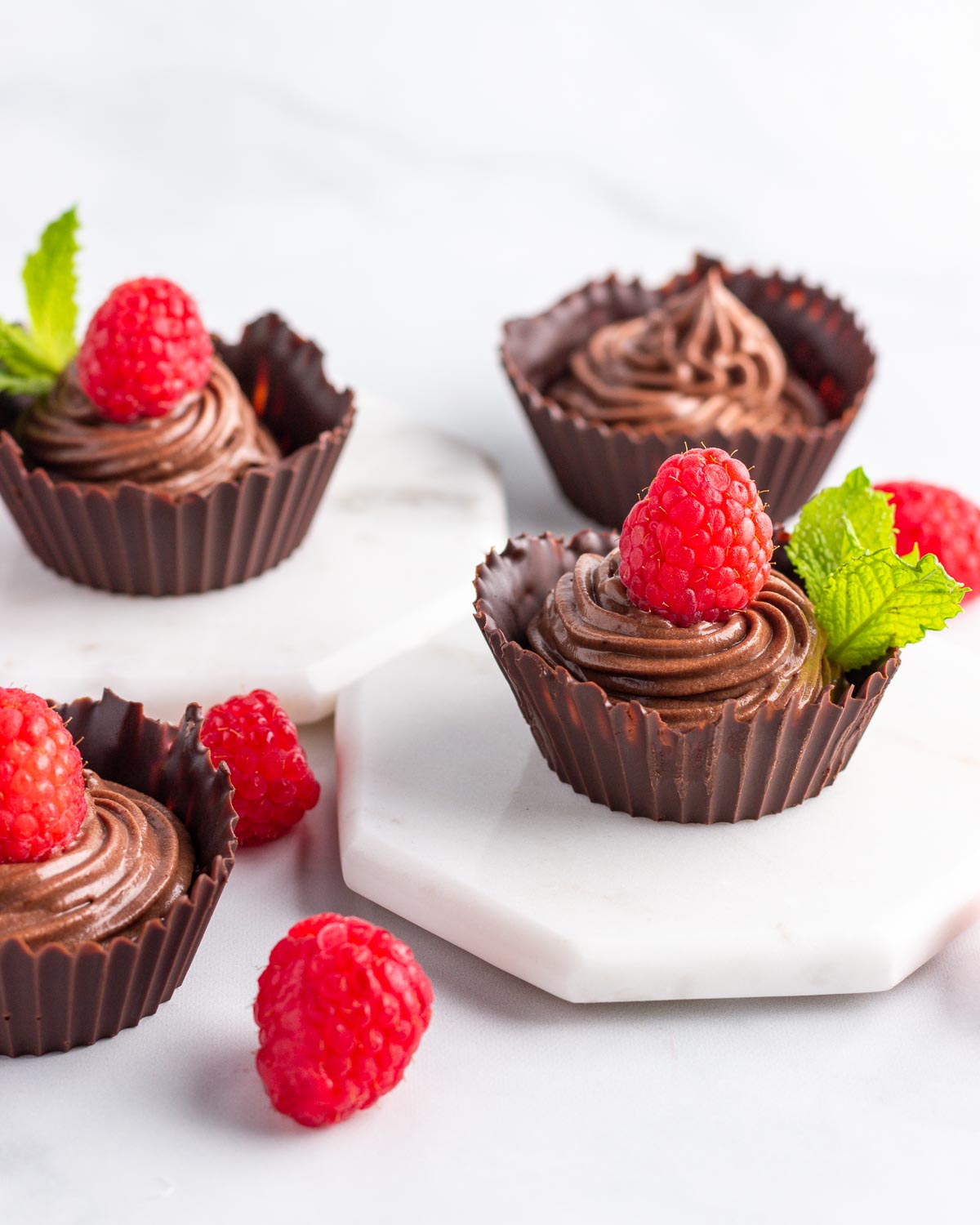Four chocolaet cups filled with chocolate mousse and topped with a raspberry.
