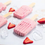 Low carb strawberry cream popsicles on white background with sliced berries and ice cubes.