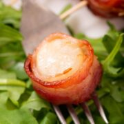 A fork with a bacon wrapped scallop on it.