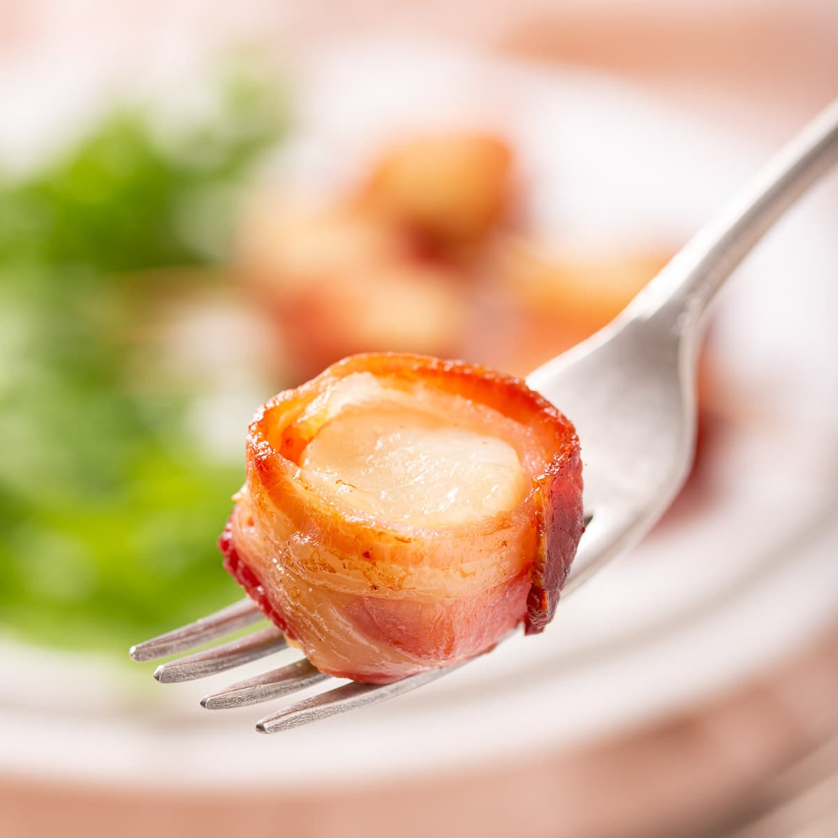 A fork with a bacon wrapped scallop on it