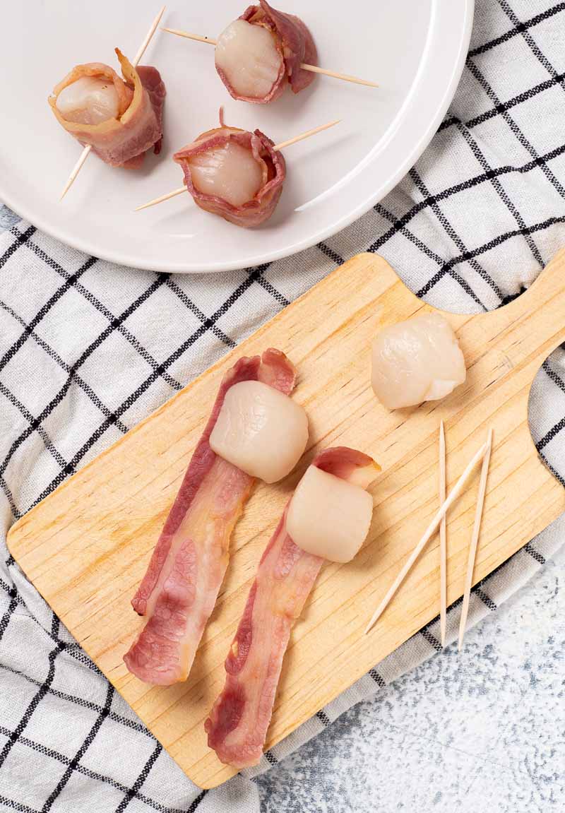 Wrapping the scallops in bacon and securing with a toothpick.