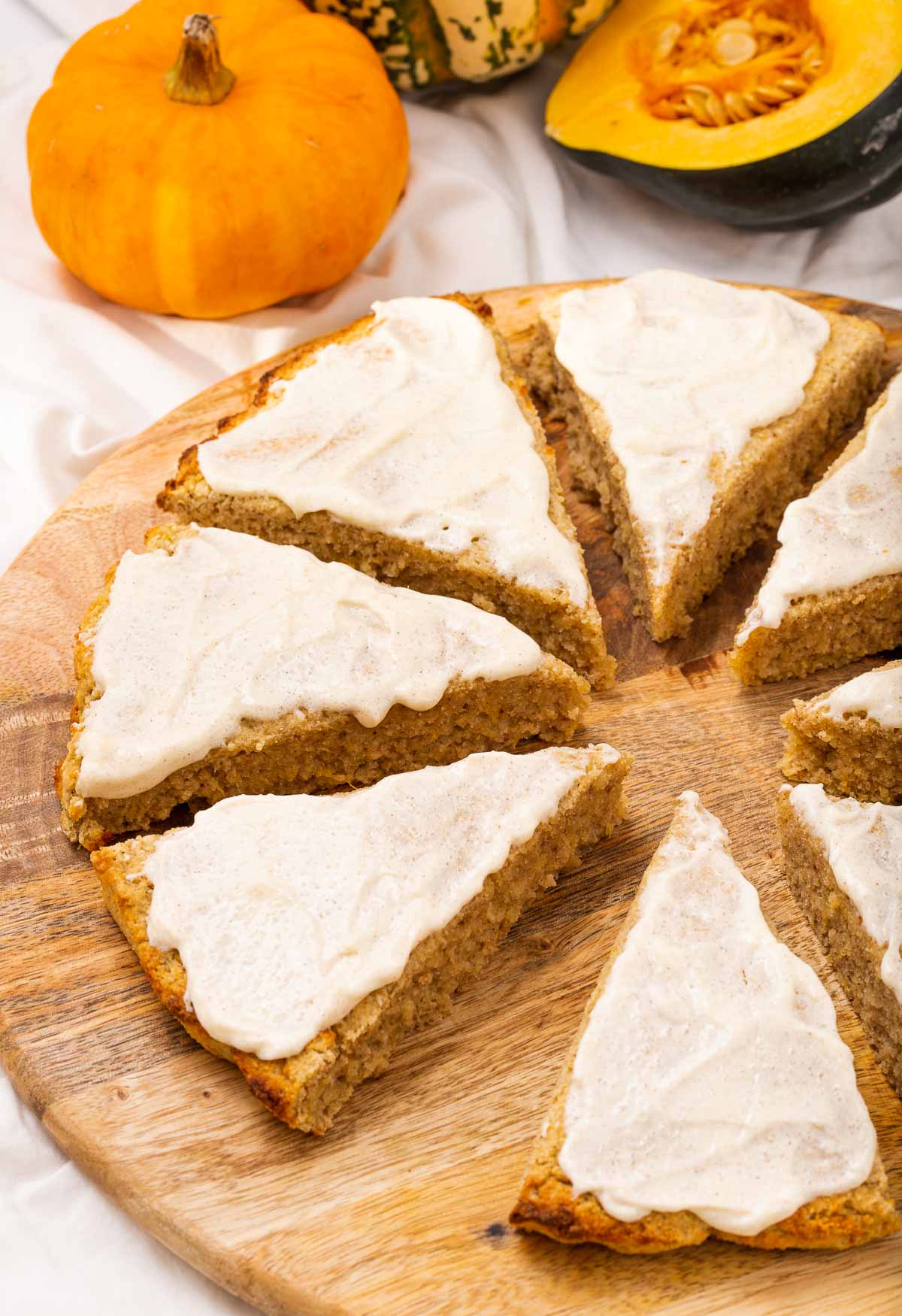 Eight pumpkin scone with vanilla icing on a cutting board.