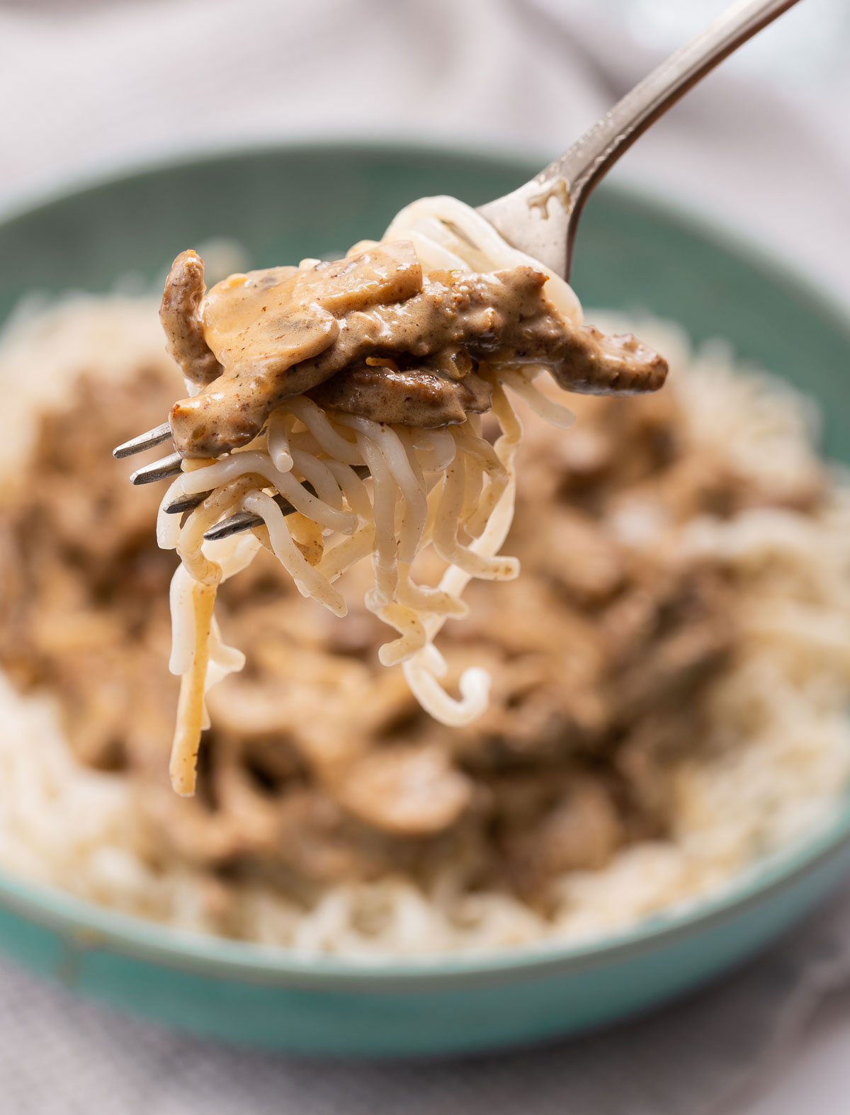 A fork holding beef stroganoff and noodles over a bowl of beef stroganoff.