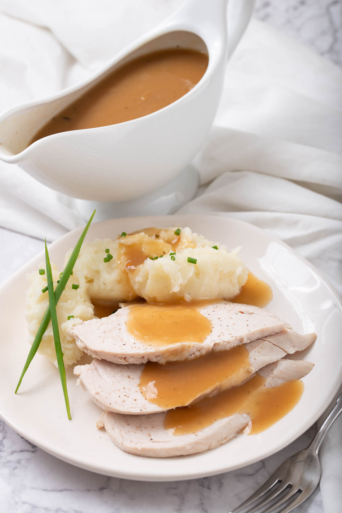 A gravy boat filled with turkey gravy and roast turkey in the background.