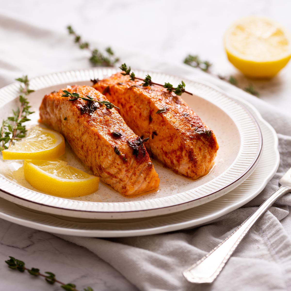 Two air fried salmon fillets on a white plate garnished with lemon slices and  thyme leaves.