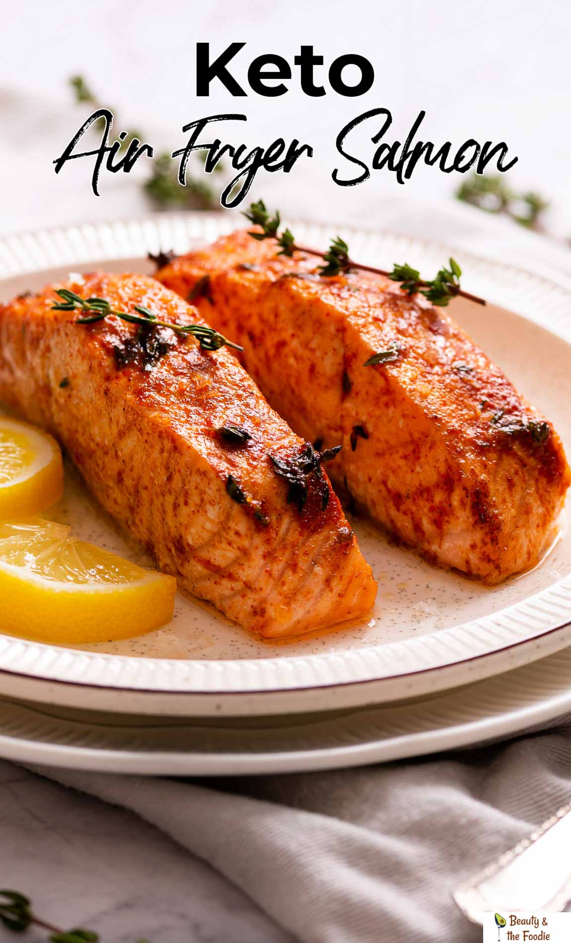 Two air fried salmon fillets on a white plate garnished with lemon slices and thyme leaves.
