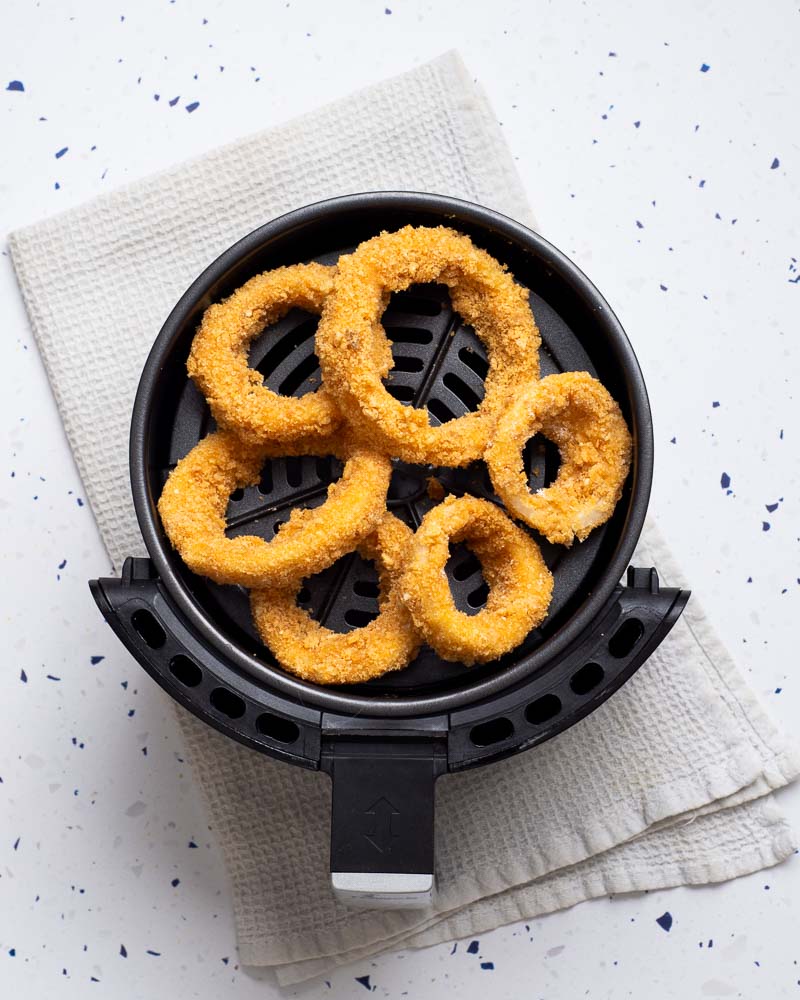 Placing the onion rings into the air fryer basket.