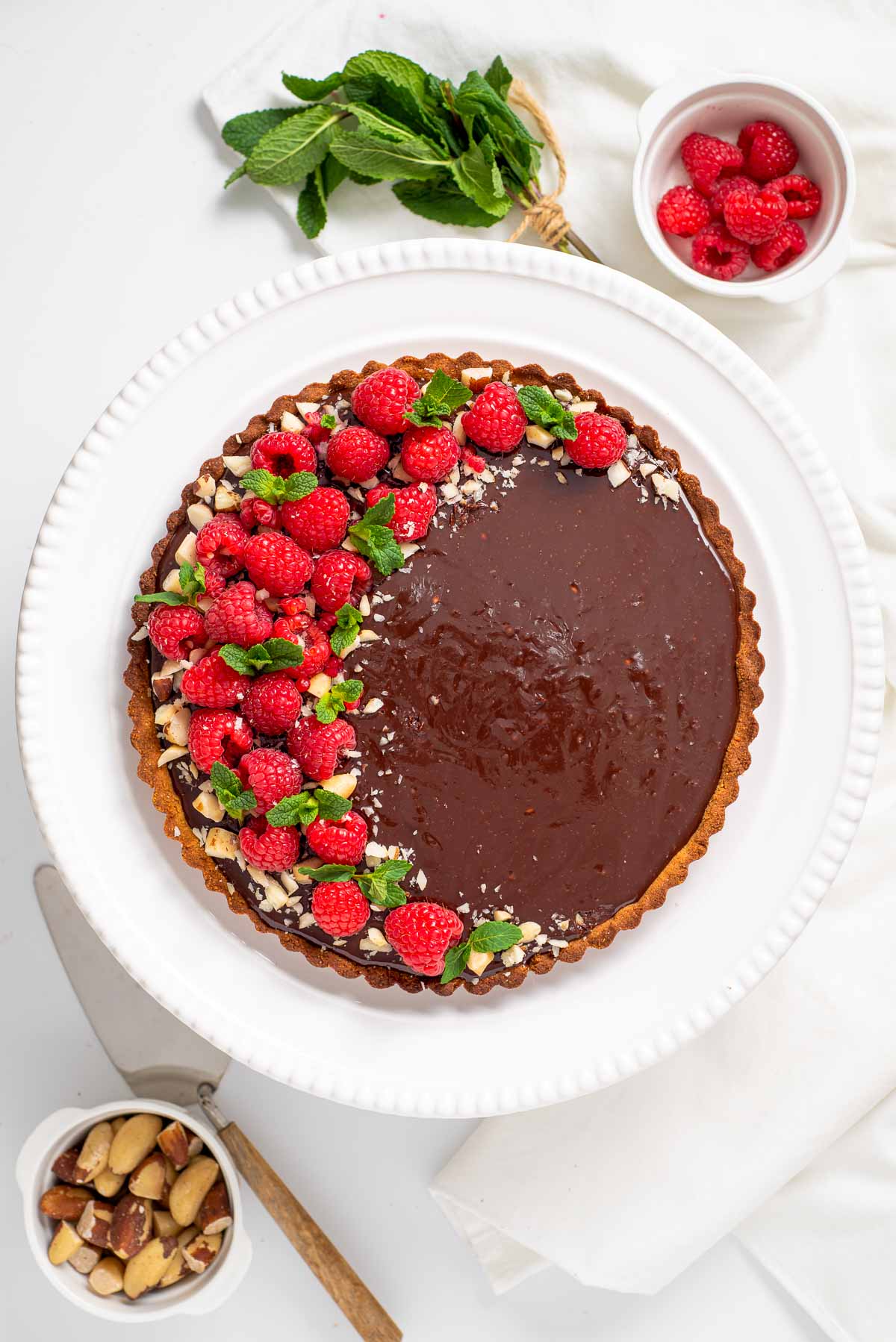 A chocolate raspberry tart taht is low carb with a bowl of berries in the background.