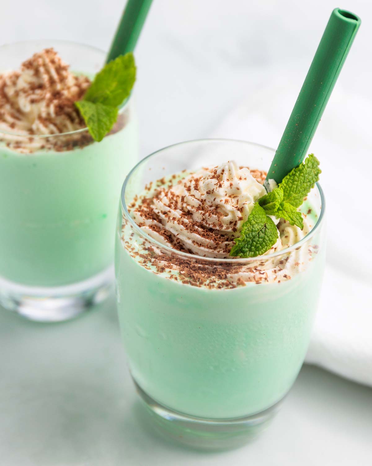 Two keto Shamrock milkshakes with whipped cream and chocolate shavings on top and a green straw.