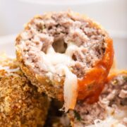 A stack of keto cheese stuffed air fryer meatballs with one meatball cut in half and cheese oozing out.