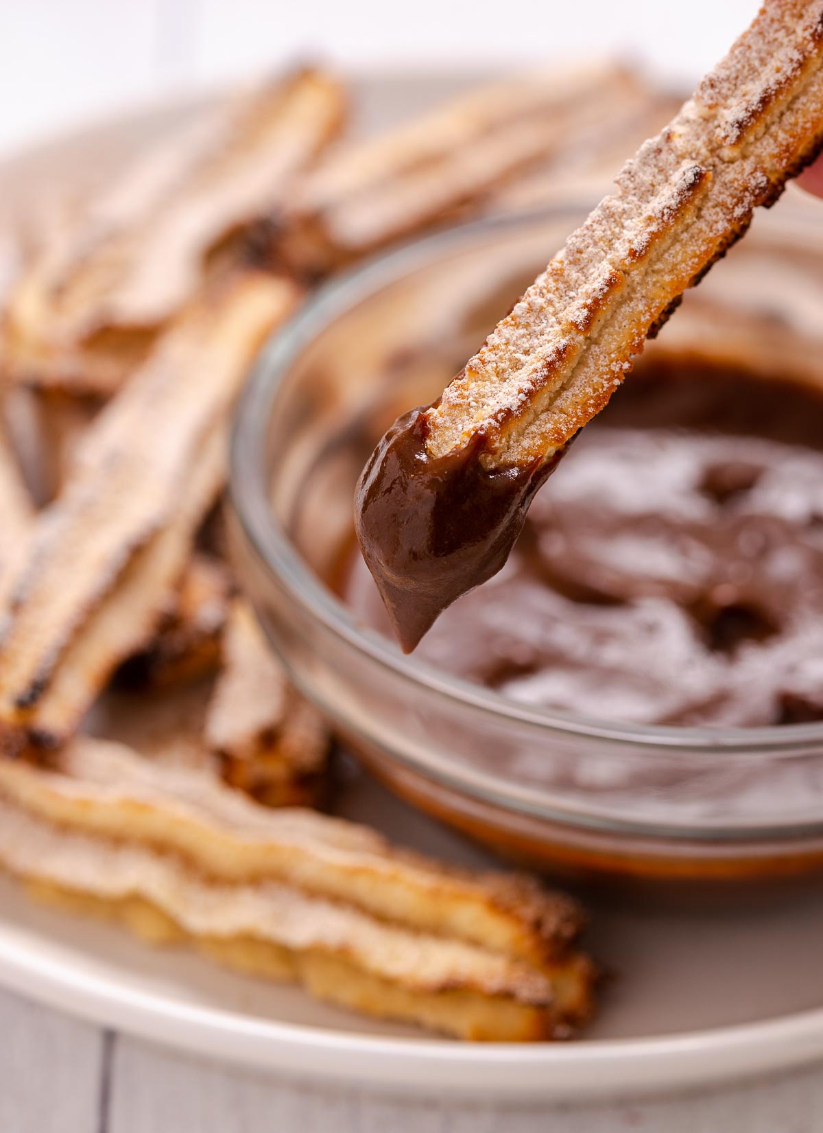 A plate of churros with one churro being dipped into a small bowl of melted chocolate.
