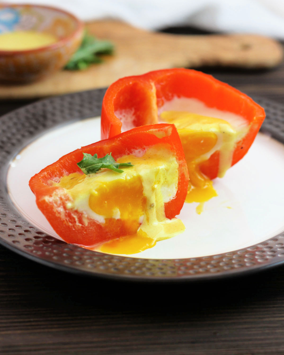 Eggs in a bell pepper cup with hollindaise sauce and cut inhalf with yolk rrunning on a bed of arugula leaves.