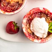 Two strawberry rhubarb crisps in a ramekin with a scoop of ice cream on one .