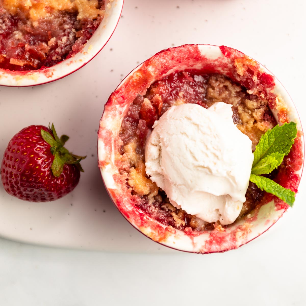 Two strawberry rhubarb crisps in a ramekin with a scoop of ice cream on one .