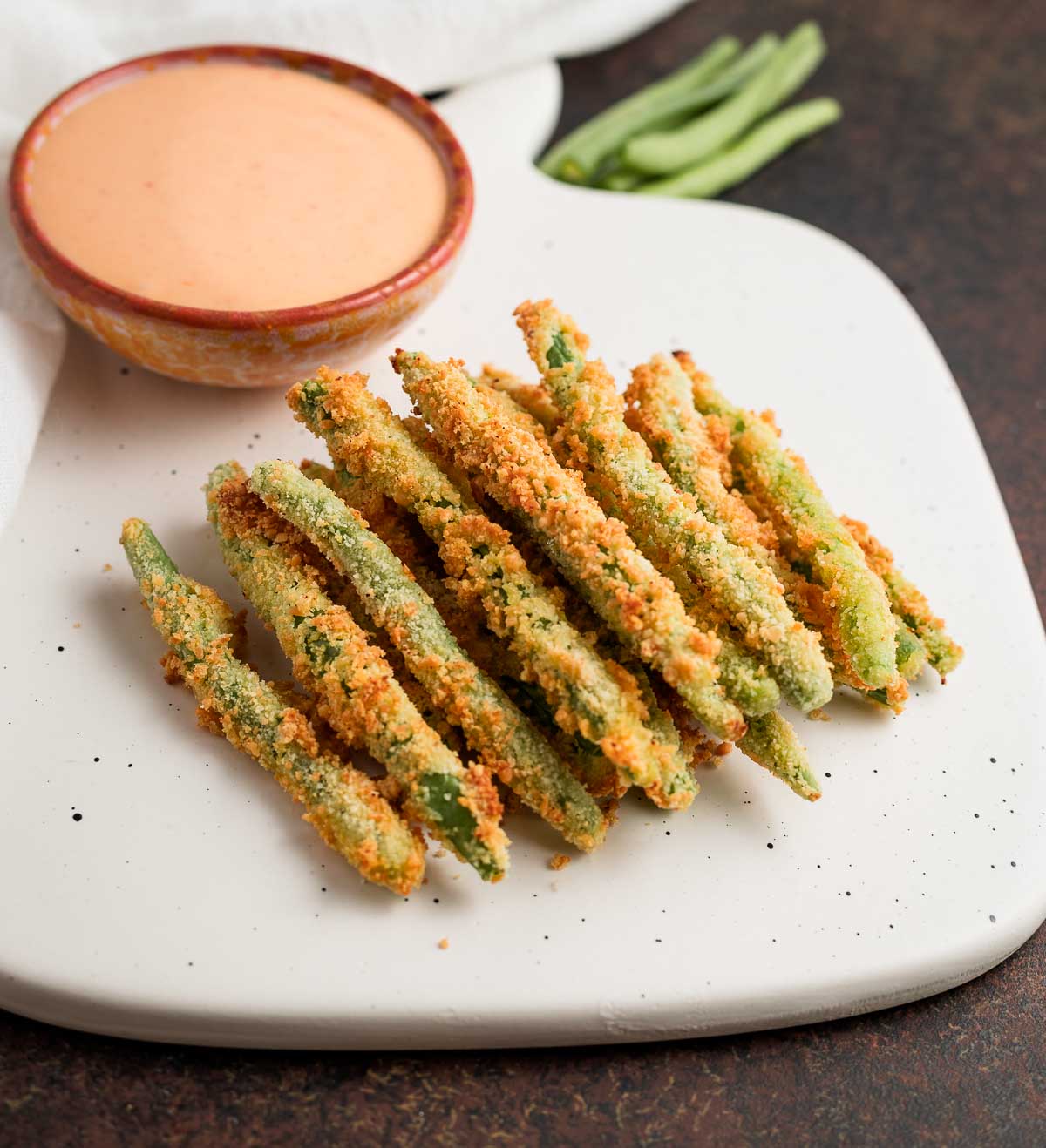 A stack of air fried green beans with a creamy dip behind them.