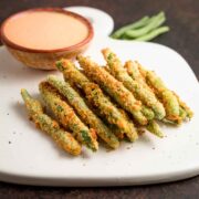 A stack of air fried green bean fries with dipping sauce in back of them.