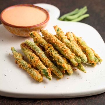 A stack of air fried green bean fries with dipping sauce in back of them.