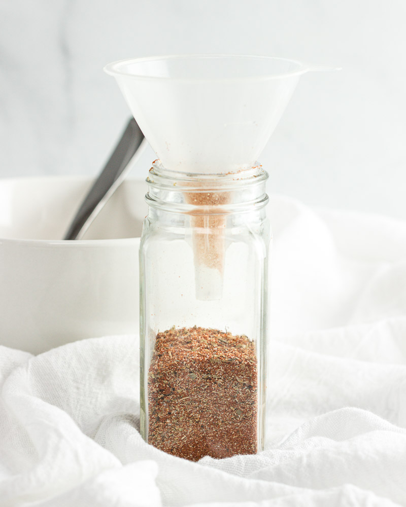Pouring spice mix into a jar with a funnel.