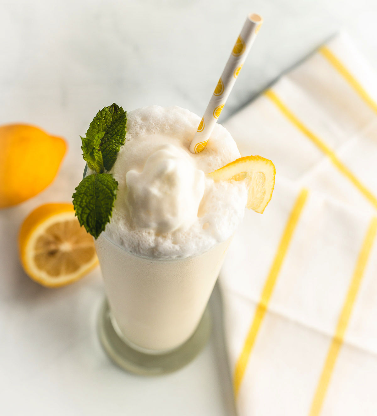 A Keto Frosty Lemonade Whip wih paper straw and lemon garnish.