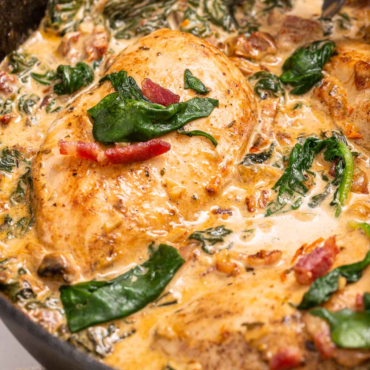 A close-up of a pan with chicken, bacon, spinach and a creamy Tuscan sun-dried tomato sauce.