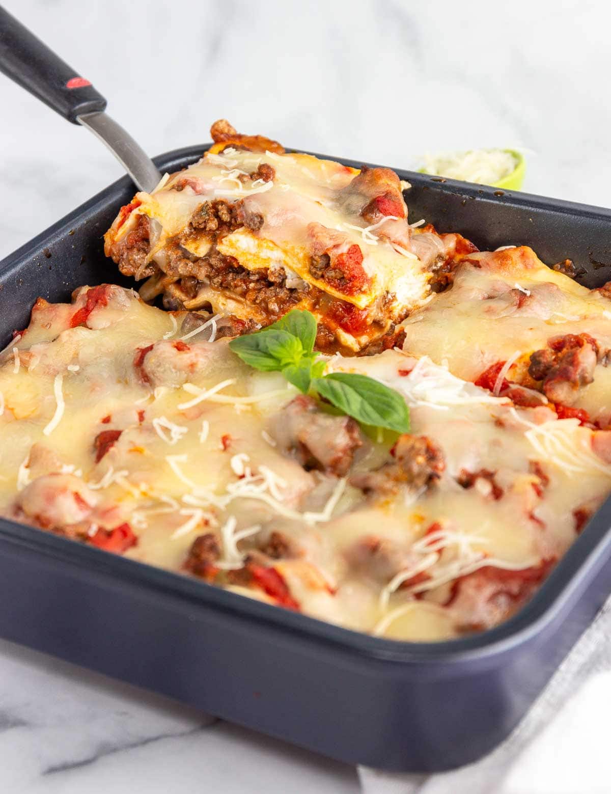 A paan of keto lasagna with a spatula lifting out a square of lasagna.