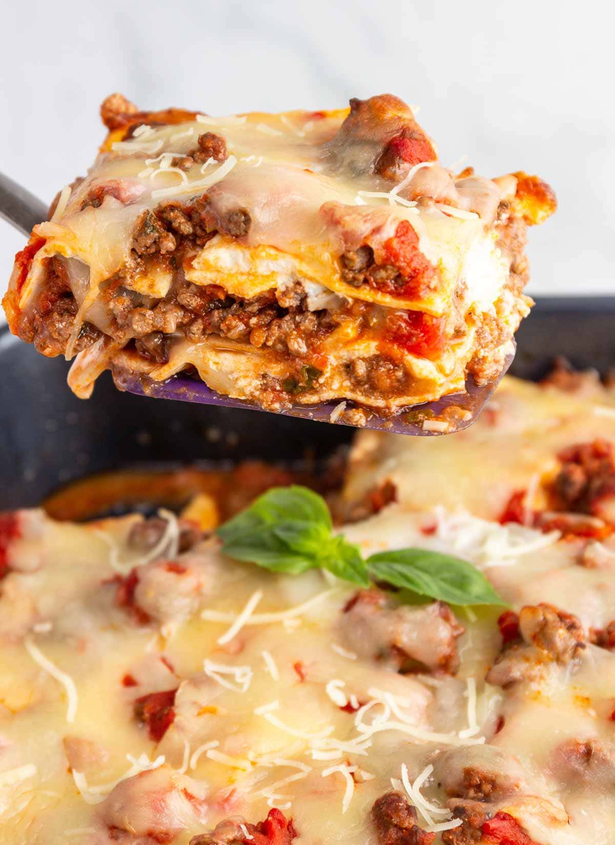 Lifting a square of cheesy meat lasagna out of a pan.