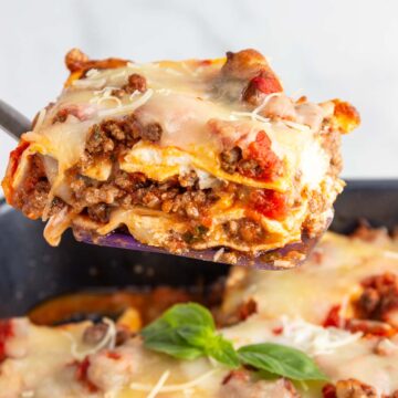 Lifting a square of cheesy meat lasagna out of a pan.