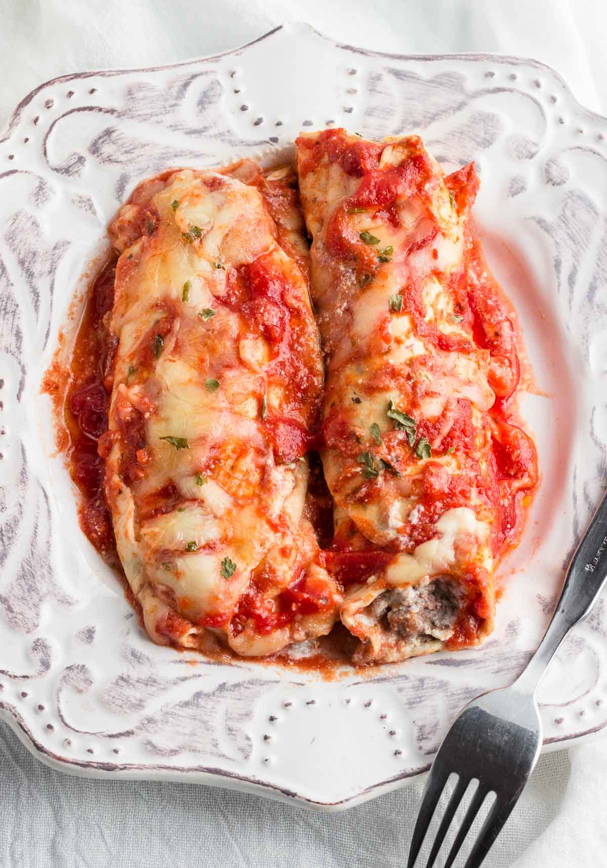 Two low carb beef and cheese manicotti rolls in sauce.