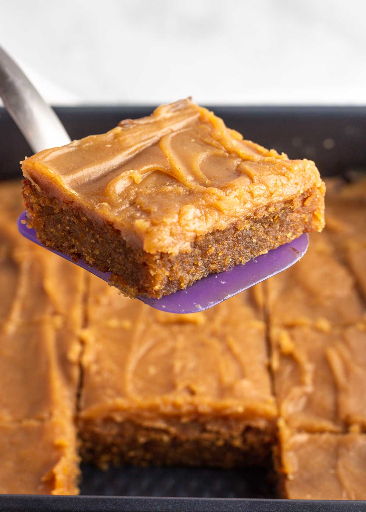 A keto iced peanut butter bar being lifted out of a pan with a spatula.