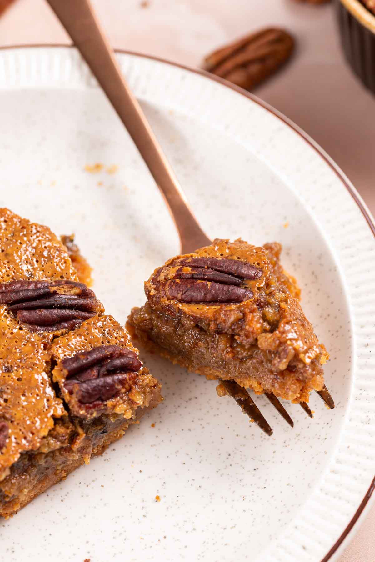 A fork cutting a bite out of a slice of pecan pie.