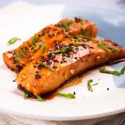 Two salmon fillets with a maple ginger glaze and garnished with black sesame seeds and green onion.