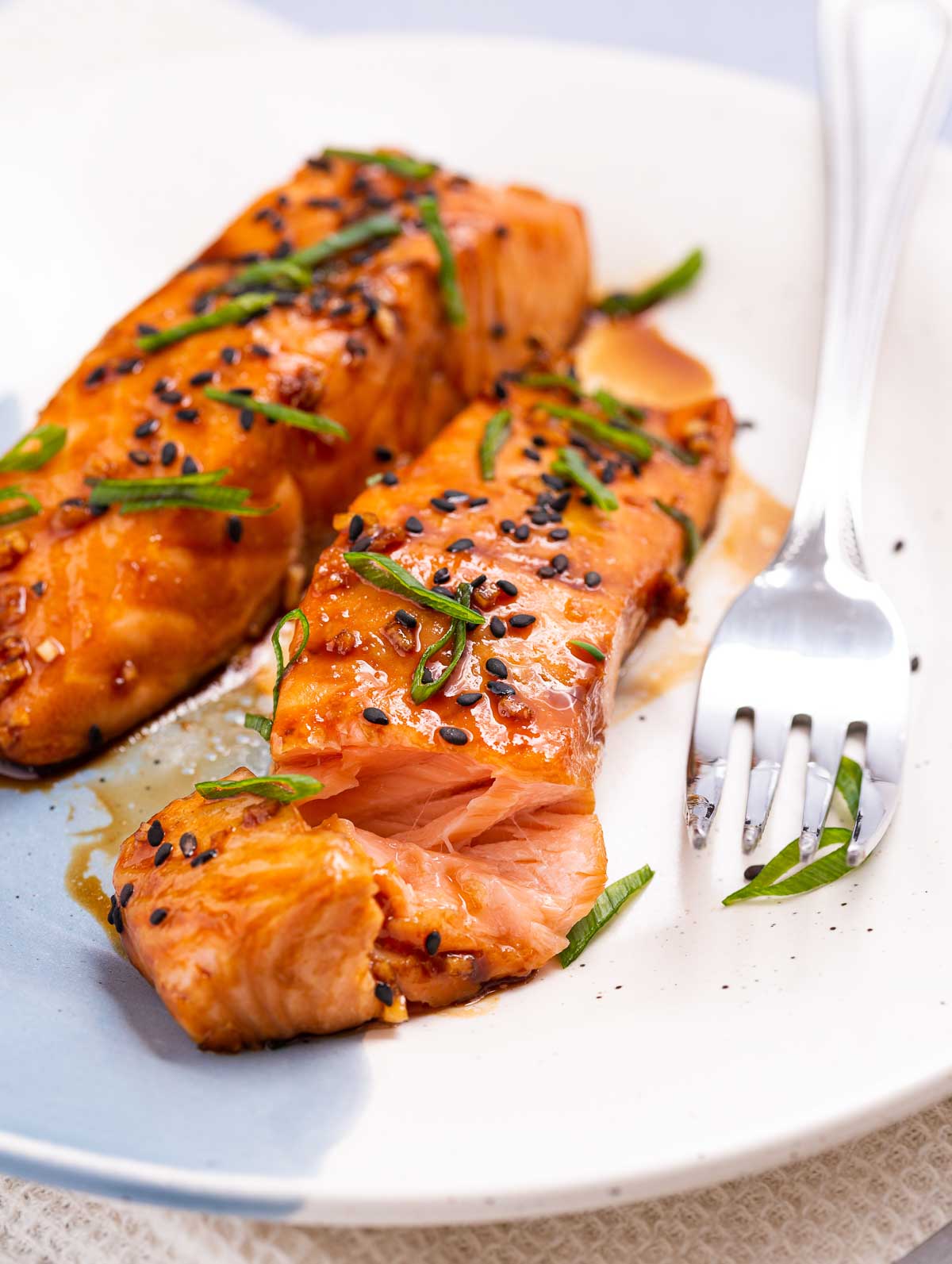 Two salmon fillets with a maple ginger glaze and garnished with black sesame seeds and green onion.
