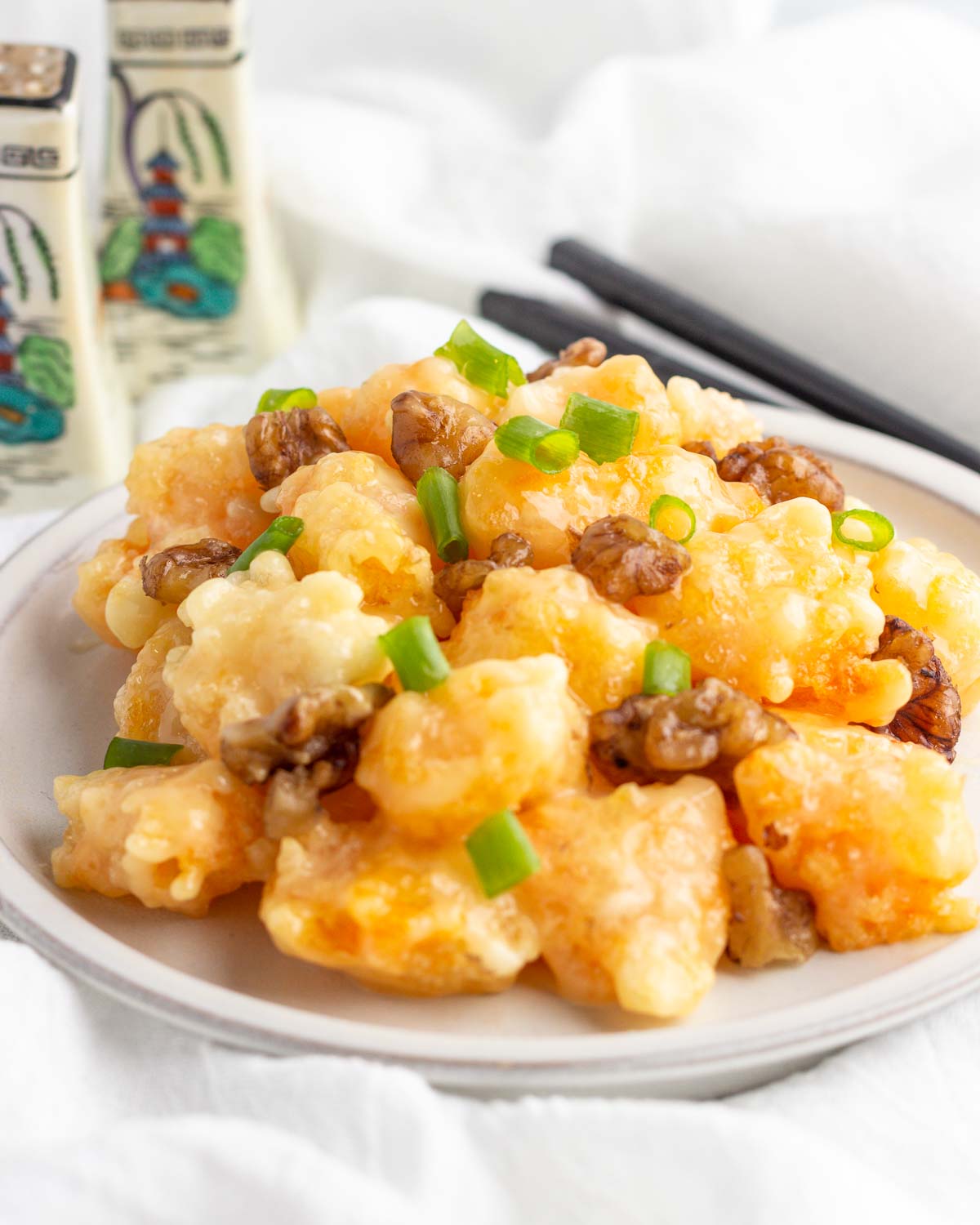 A plate of honey walnut shrimp with a green onion garnish on a plate.