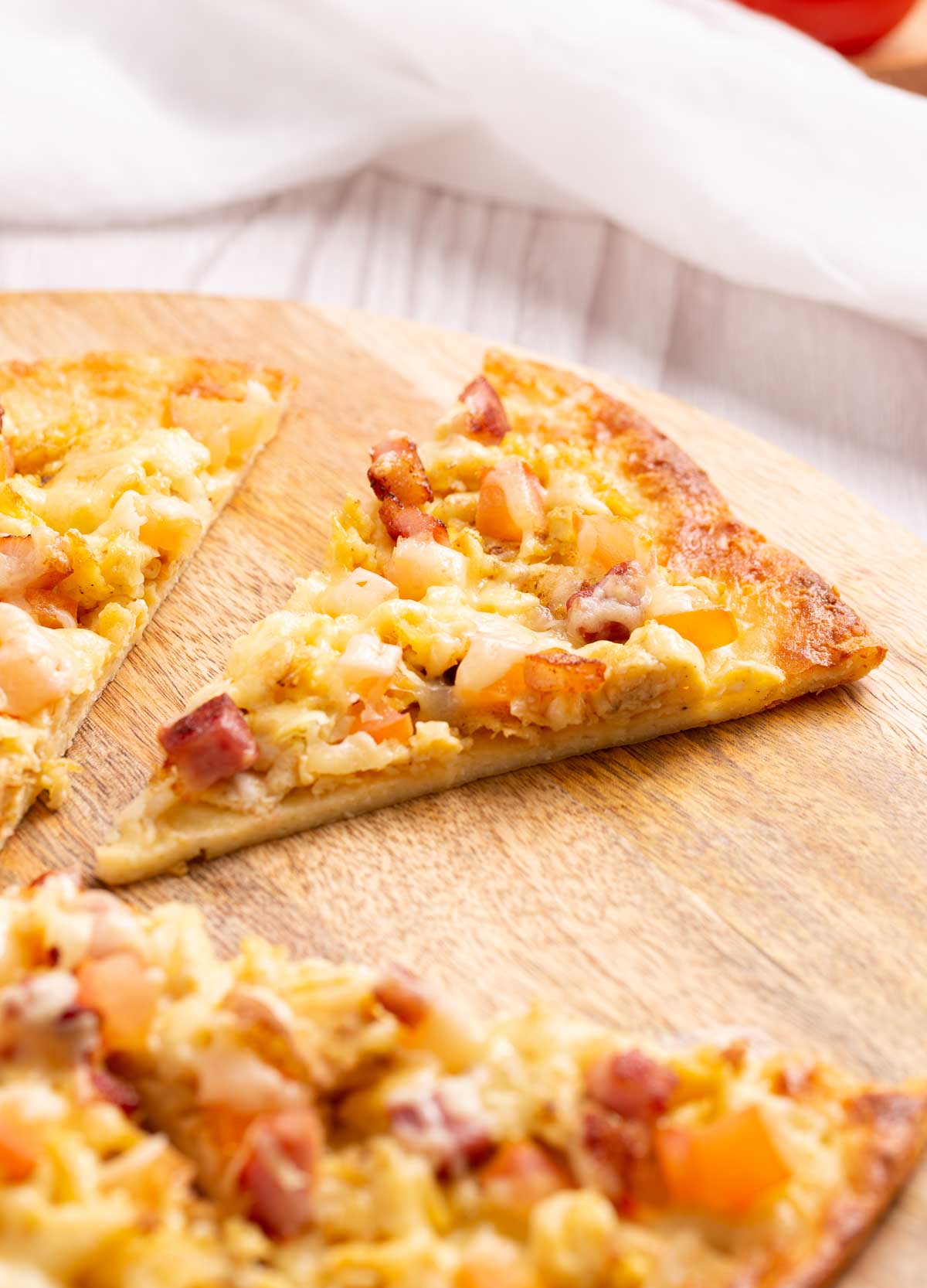A slice of breakfast pizza with scrambled eggs, bacon, cheese and tomato.