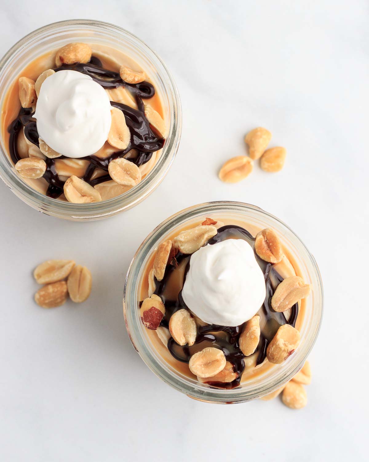 Two cups of keto peanut butter cheesecake mousse with chocolate and caramel syrup and peanuts.