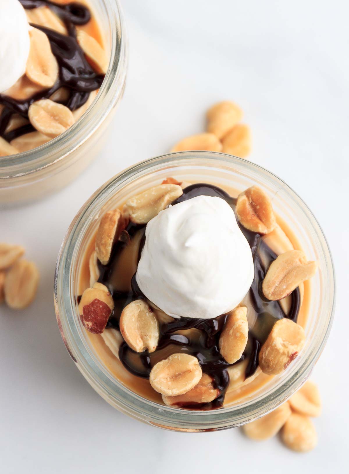 Two cups of keto peanut butter cheesecake mousse with chocolate  and caramel syrup and peanuts.