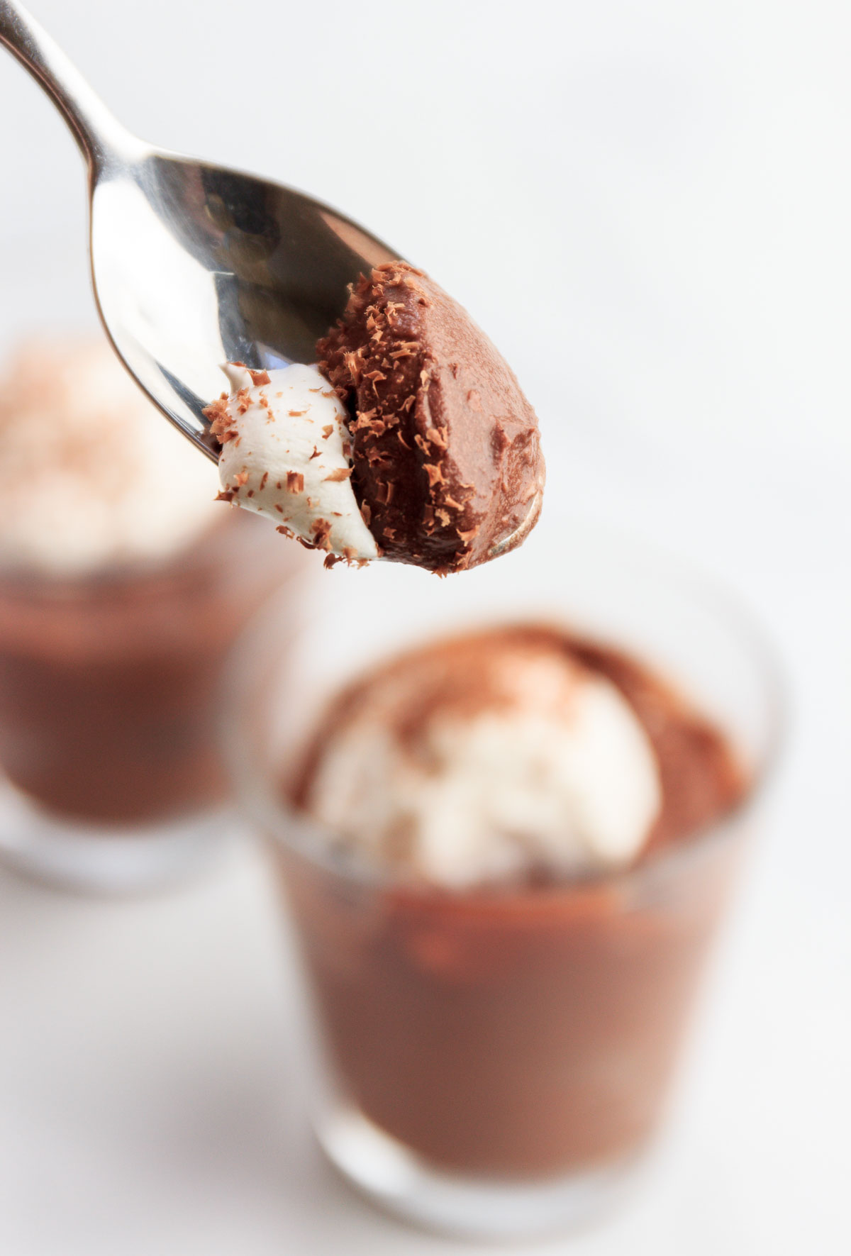 A spoonful of chocolate coconut mousse and whipped cream coming out of a dessert glass.