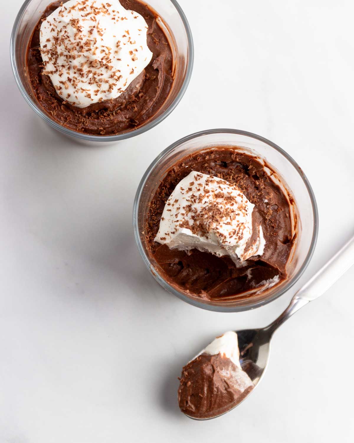 Two small glasses of keto chocolate coconut mousse with whipped cream and a spoonful of it next to the glass.