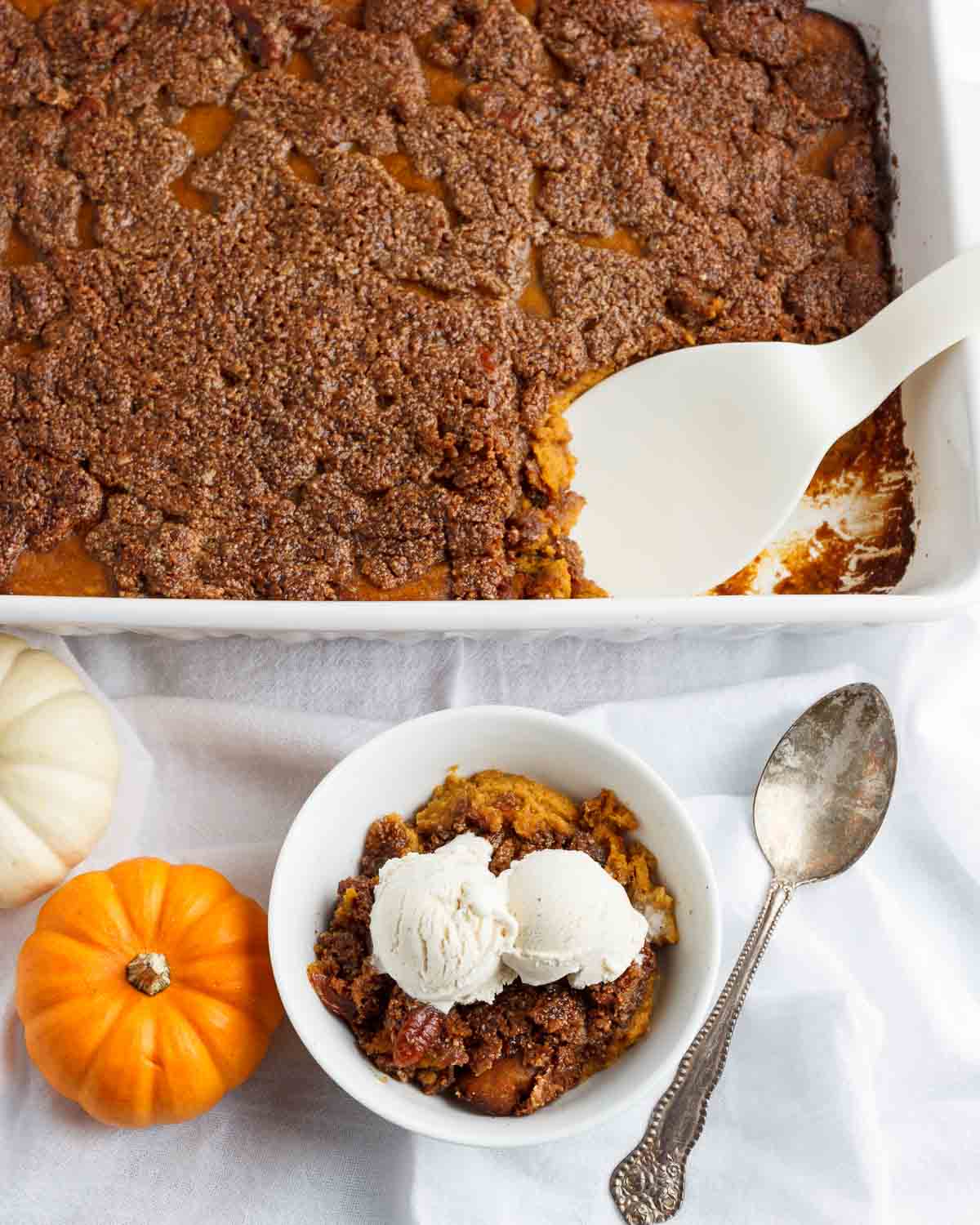A dish of pumpkin crisp with a serving bowl in front with the pumpkin crisp and ice cream on top.