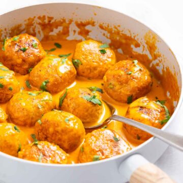 A skillet with butter chicken meatballs in creamy sauce.