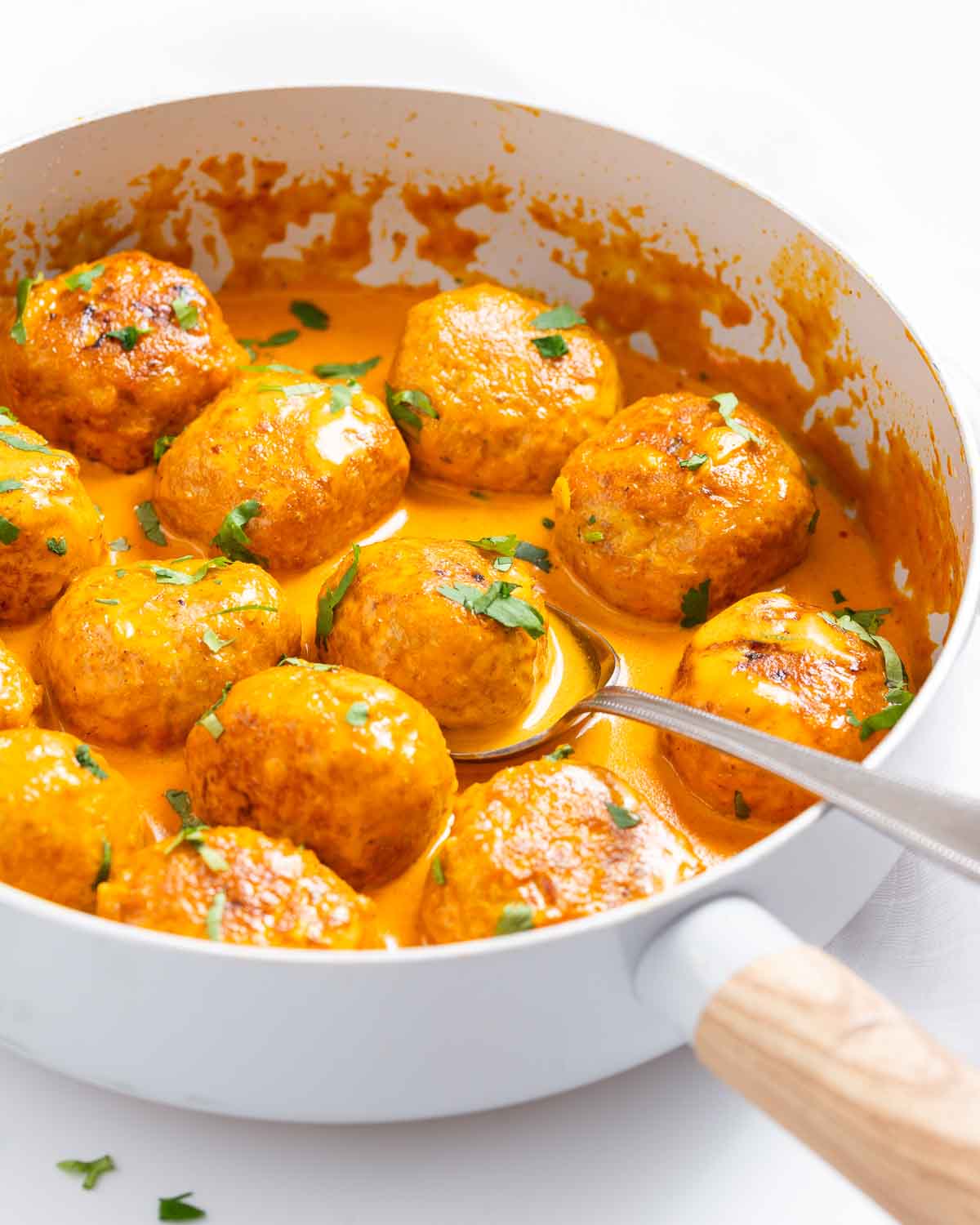 A skillet with butter chicken meatballs in creamy sauce.