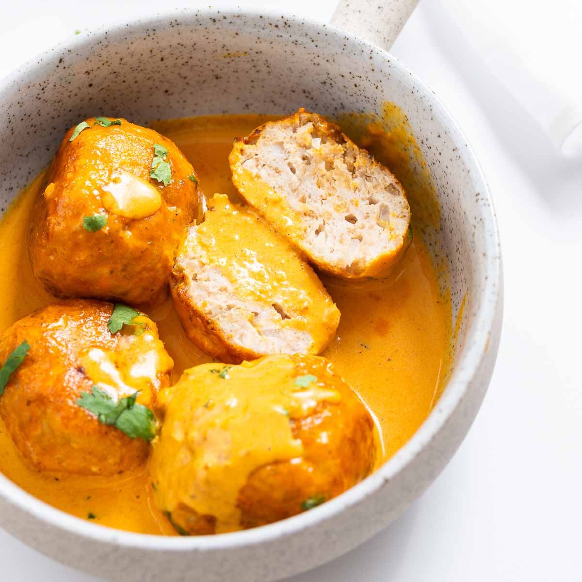 A bowl of butter chicken meatballs in a creamy sauce.
