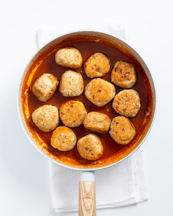 Adding meatballs to the sauce to simmer.